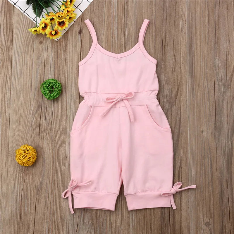 Pink romper with straps on a wooden surface with decorative elements.