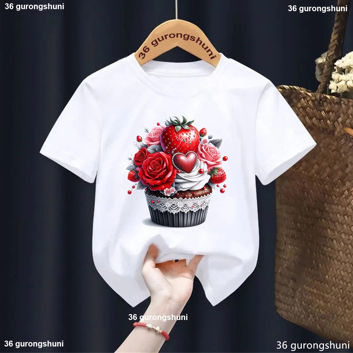 White t-shirt with a cupcake and floral design on a hanger against a dark background.