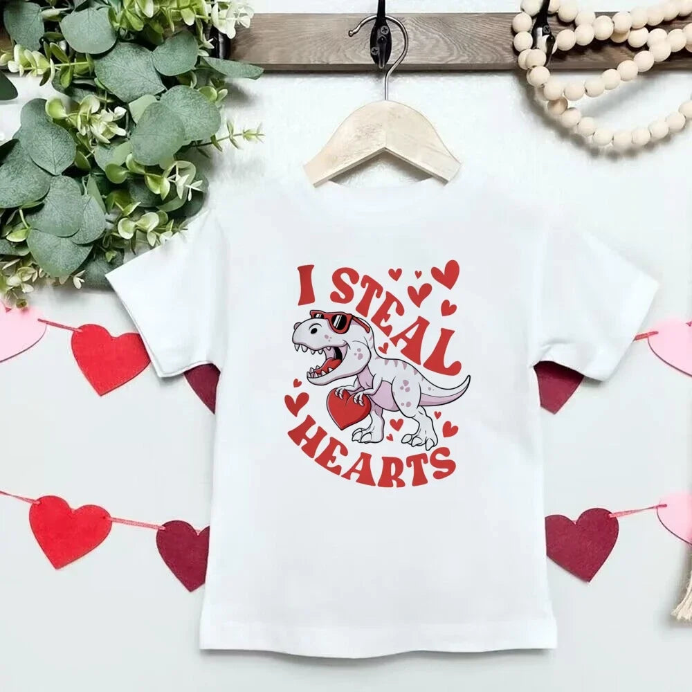 White t-shirt with a dinosaur graphic and 'I Steal Hearts' text on a hanger with decorative elements.