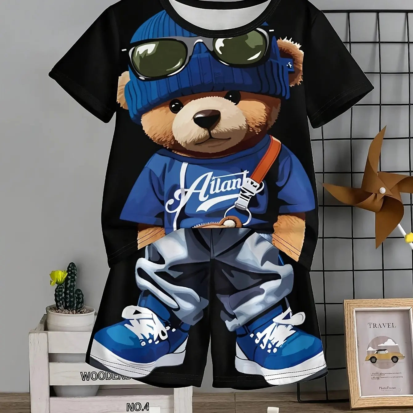T-shirt with a teddy bear design wearing sunglasses, a beanie, and sneakers on a black background.