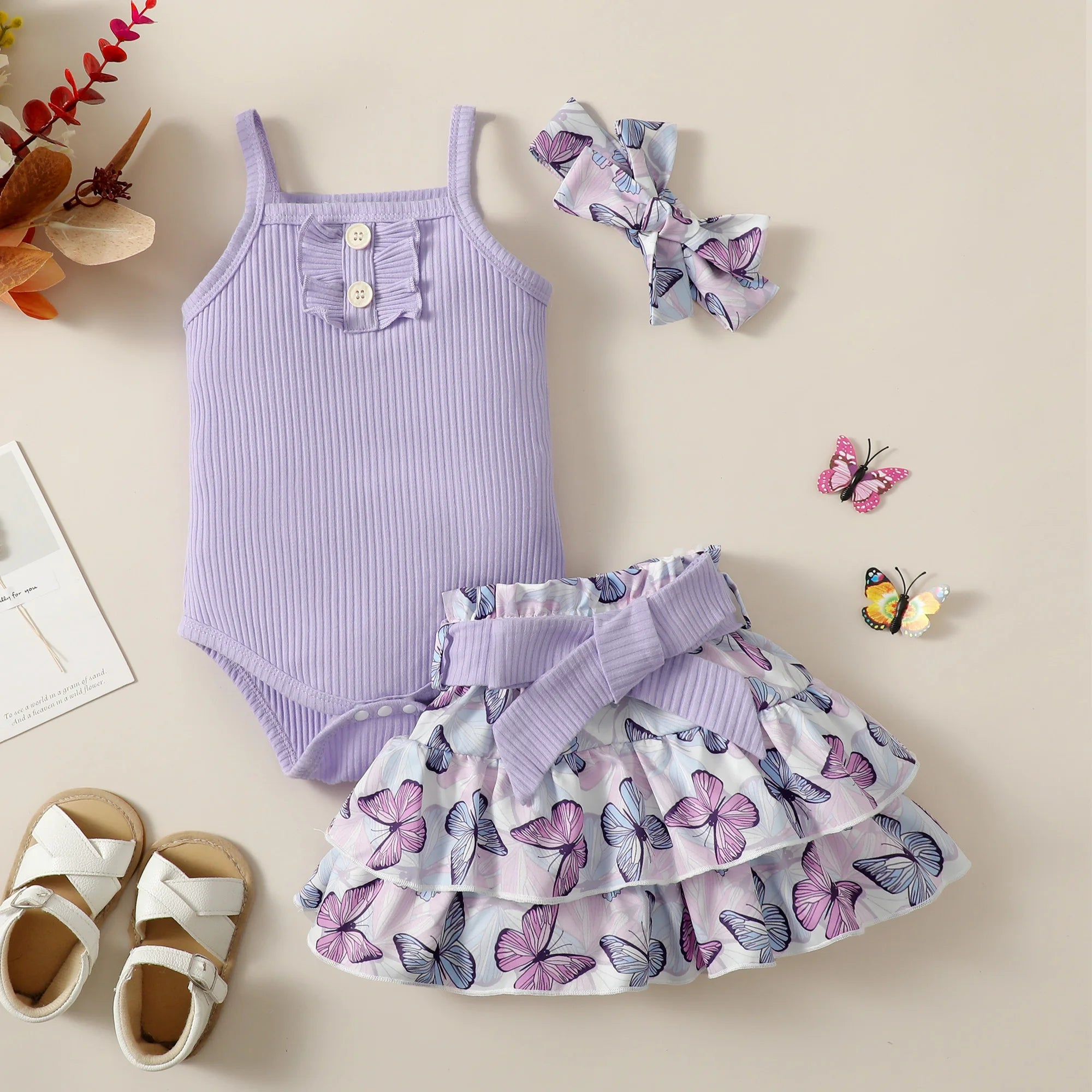 Children's outfit set with purple striped romper, skirt, headband, and shoes on a beige background.