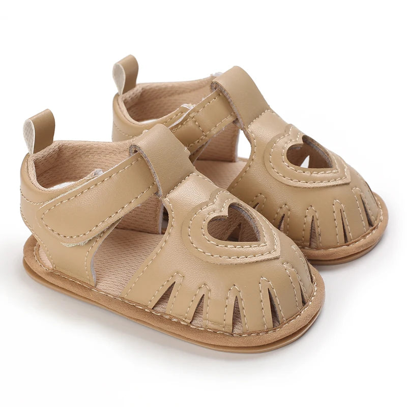 Pair of beige baby sandals with heart designs on a white background