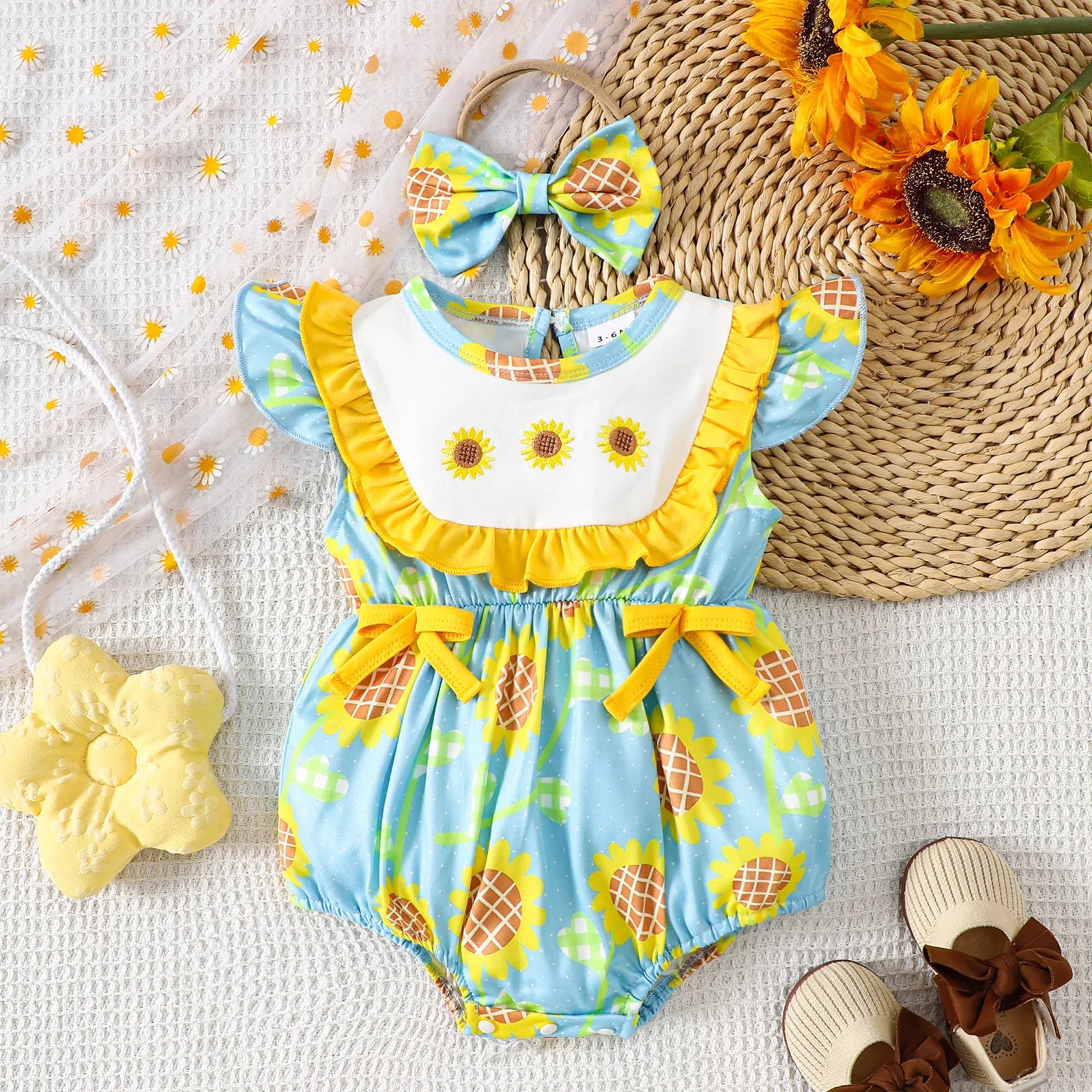 Baby romper with sunflower pattern, headband, and sandals on a textured surface.
