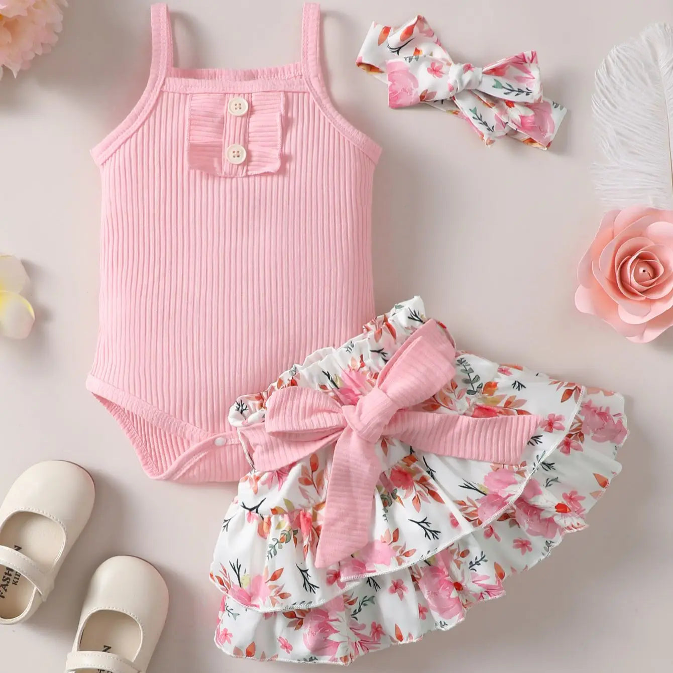 Pink baby romper with floral shorts and headband on a light background