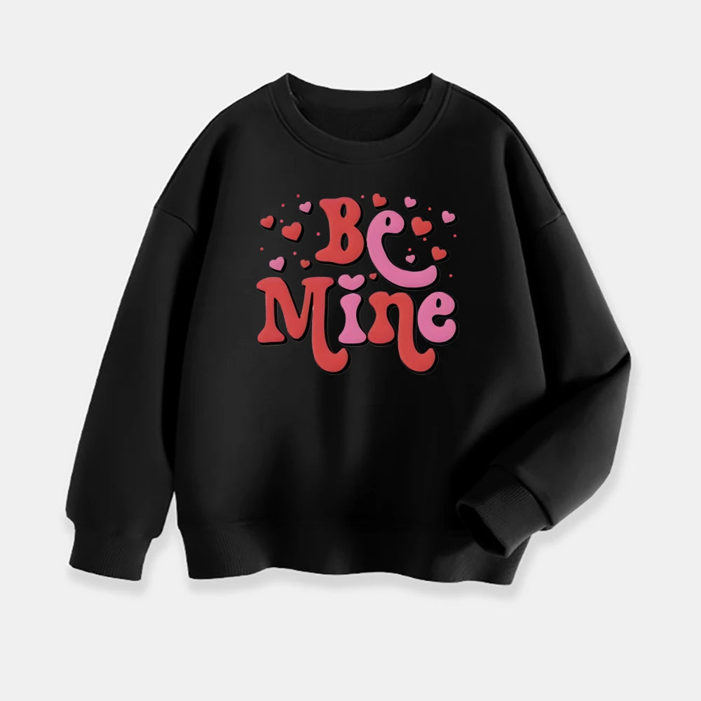 Black sweatshirt with 'Be Mine' text and hearts on a light gray background