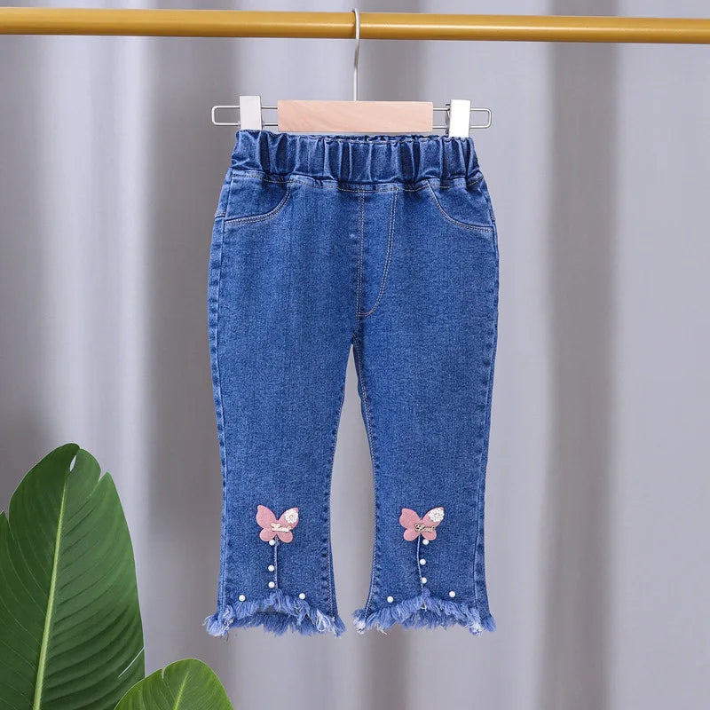 Blue denim pants with butterfly designs on a hanger against a gray background
