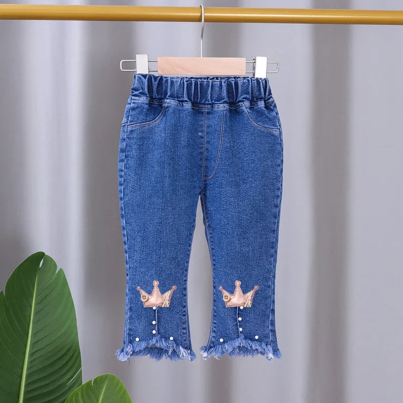 Blue denim pants with crown designs on a hanger against a gray background