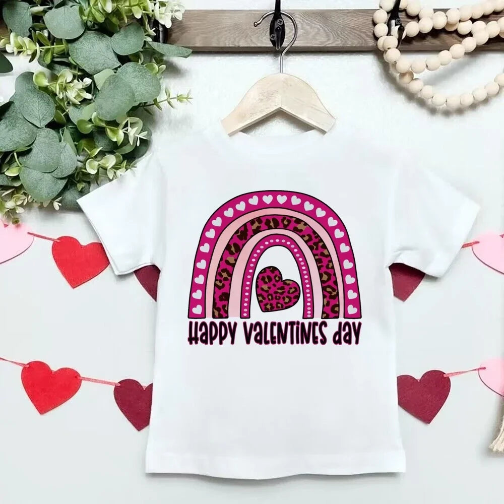White t-shirt with a pink rainbow and heart design on a hanger with decorative elements.