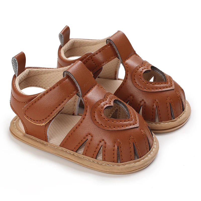 Pair of brown baby sandals with heart designs on a white background