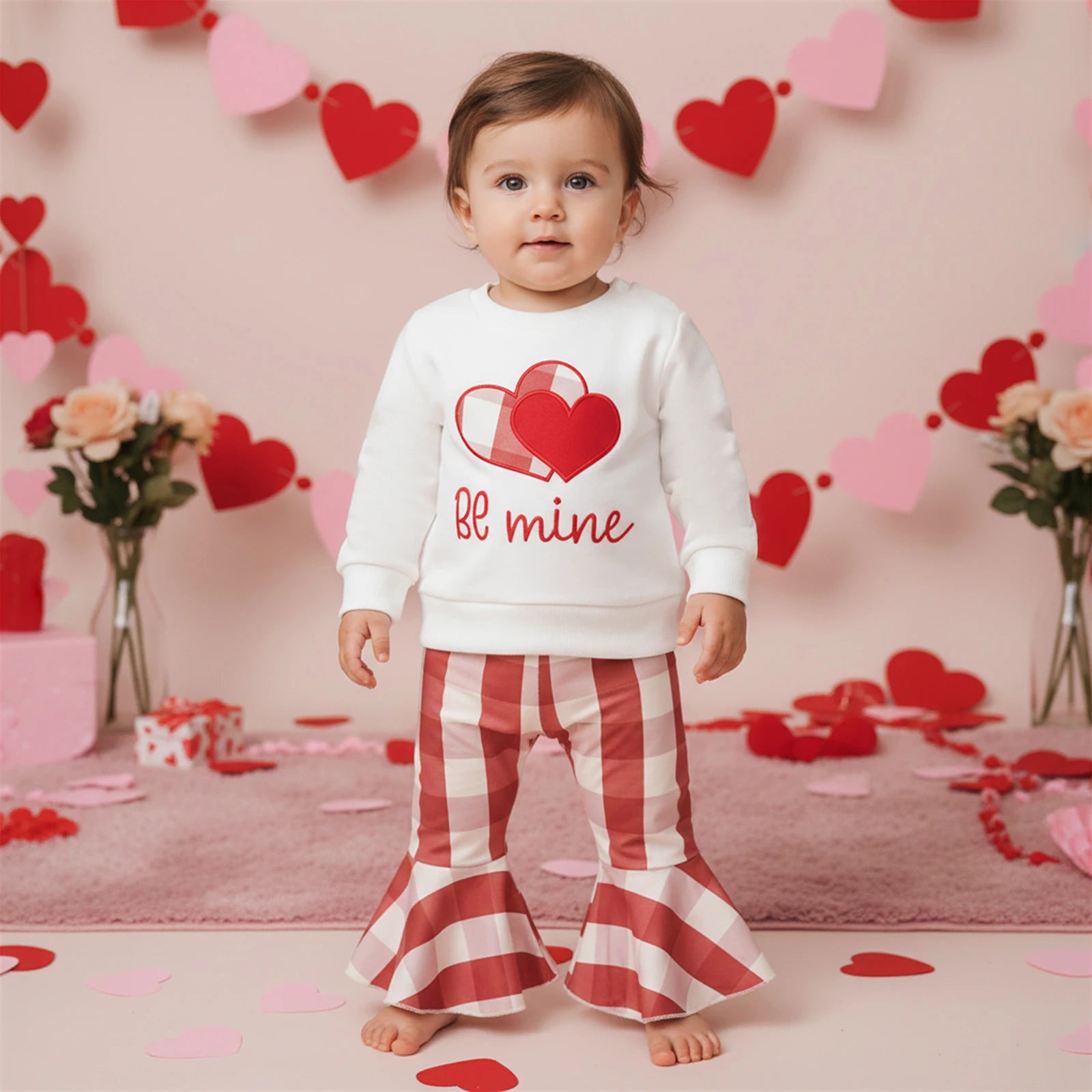 Child wearing a Valentine's Day-themed outfit with a heart design and 'bf mine' text, standing in a decorated room with heart decorations.